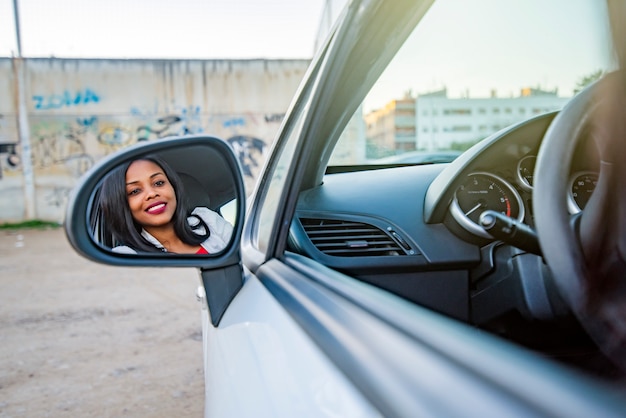 Schöne lächelnde afroamerikanische Frau in einem Auto, das in einem der Außenspiegel reflektiert wird