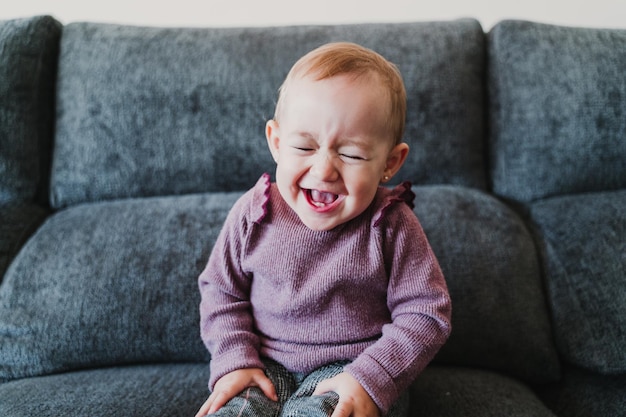 Schöne lächelnde Baby-Mädchen sitzt zu Hause auf dem Sofa