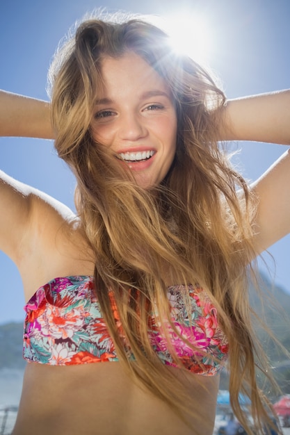 Schöne lächelnde Blondine im Blumenbikini auf dem Strand
