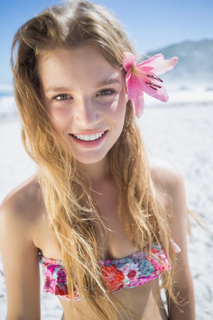 Schöne lächelnde Blondine mit Blumenhaarzusatz auf dem Strand