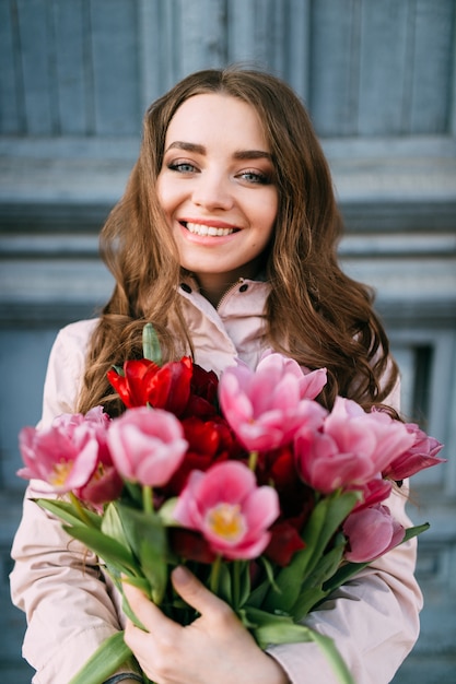 Schöne lächelnde brünette Frau, die vor alter Tür mit einem Strauß frischer Tulpen steht.