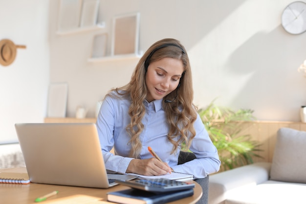 Schöne lächelnde Callcenter-Mitarbeiterin mit Kopfhörern arbeitet im Home Office.