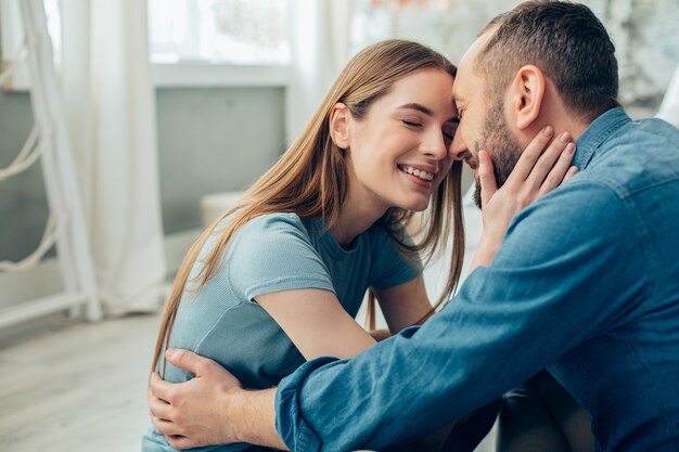 Schöne lächelnde Dame, die ihre Augen schließt und ein Gesicht ihres fröhlichen Freundes berührt