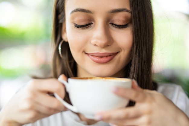 Schöne lächelnde Frau, die Kaffee im Café trinkt. Porträt einer reifen Frau in einer Cafeteria, die heißen Cappuccino trinkt und die Kamera betrachtet. Hübsche Frau mit Tasse Kaffee.