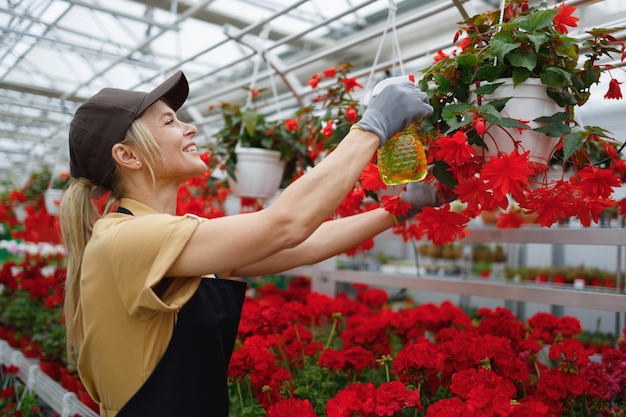 Schöne lächelnde Frau, die Pflanzen im Blumenzentrum sprüht