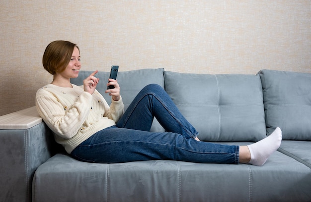 Schöne lächelnde Frau, die sich zu Hause mit dem Handy auf einer Couch entspannt