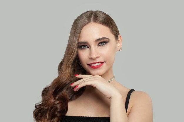 Schöne lächelnde Frau mit braunen lockigen Haaren und roten Manikürnägeln auf weißem Hintergrund