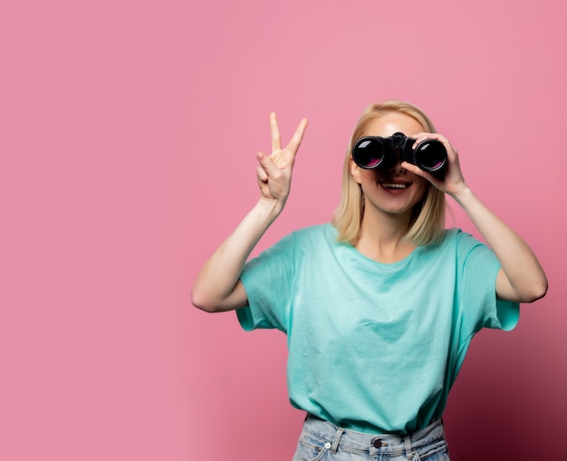 Schöne lächelnde Frau mit Fernglas auf rosa Wand