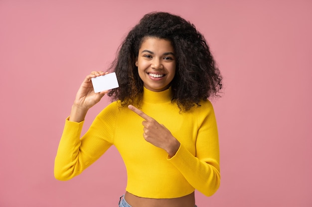 Schöne lächelnde Frau mit leerer Visitenkarte, die mit dem Finger auf den Kopierbereich zeigt Mockup