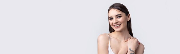Schöne lächelnde Frau mit sauberer Haut, natürlichem Make-up und weißen Zähnen auf grauem Hintergrund