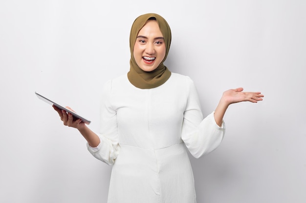 Schöne lächelnde freundliche junge arabische asiatische muslimische Frau, die hijab grün trägt und ein digitales Tablet hält und leeren Raum mit der Hand zeigt, die auf weißem Hintergrund isoliert ist Religiöses Lifestyle-Konzept der Menschen