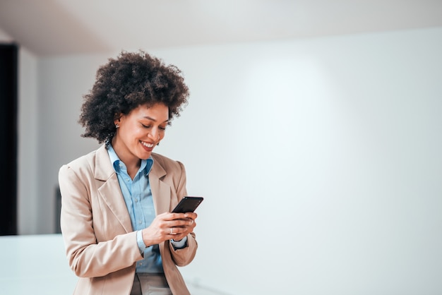 Schöne lächelnde gelockte Geschäftsfrau, die zuhause smarphone, Kopienraum verwendet.