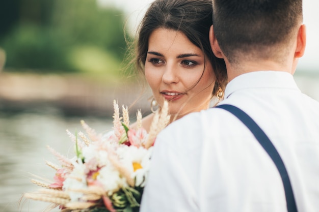 Schöne lächelnde junge Frau des Braut Brunette mit boho Artblumenstrauß mit Bräutigam