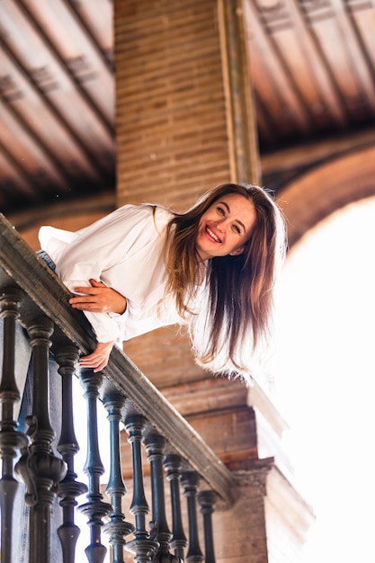 Schöne lächelnde kaukasische Frau, die sich auf das Geländer eines Balkons auf der Plaza de Espana in Sevilla lehnt