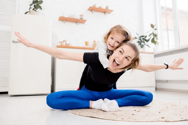 Schöne lächelnde Mutter treibt mit ihrer Tochter zu Hause Sport