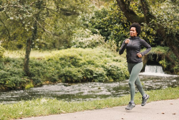 Schöne lächelnde reife Afroamerikanerin joggt entlang des Weges in der Nähe des Gebirgsflusses in der Natur.