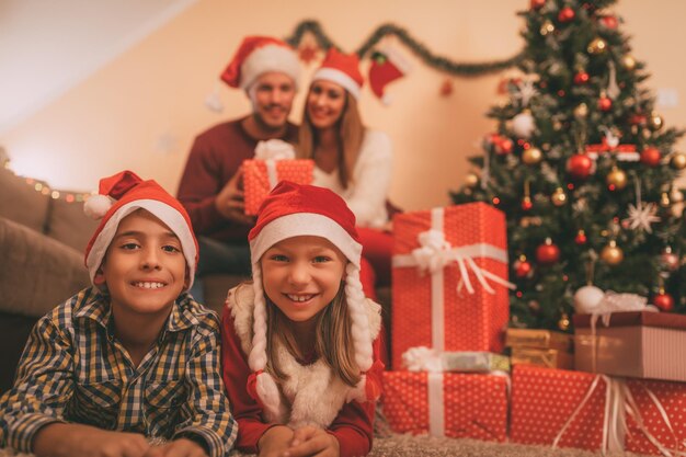 Schöne lächelnde Schwester und Bruder, die in einer Weihnachtszeit zu Hause genießen. Sie tragen Weihnachtsmützen und schauen in die Kamera. Selektiver Fokus.