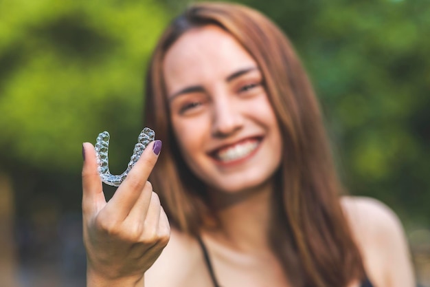 Schöne lächelnde Türkin hält eine Invisalign-Armschiene mit lebendigen Farben