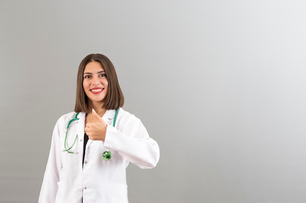 Schöne lächelnde türkische Ärztin Porträt im Studio, sie ist zuversichtlich, dass sie mit dem Daumen nach oben gestikuliert