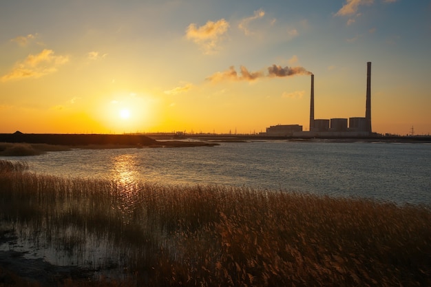 Schöne Landschaft mit Wärmekraftwerk, See und Sonnenunterganghimmel.