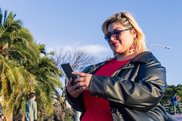 Schöne lateinische junge Frau in Übergröße, die im Freien zuschaut und Handy benutzt