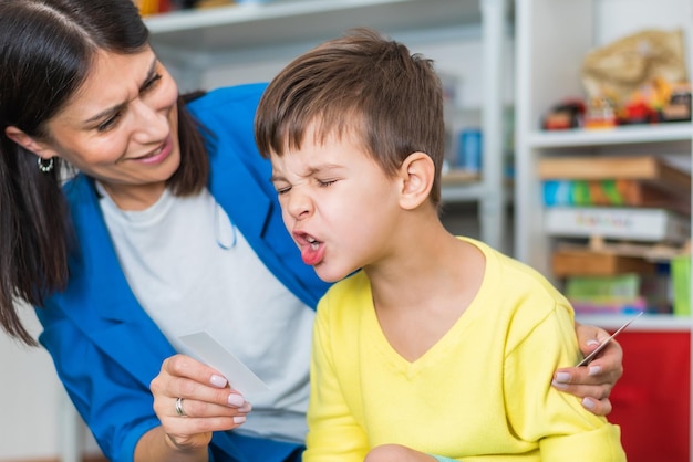 Schöne Logopädin lehrt Jungen die richtige Aussprache von Wörtern und Tönen im Büro