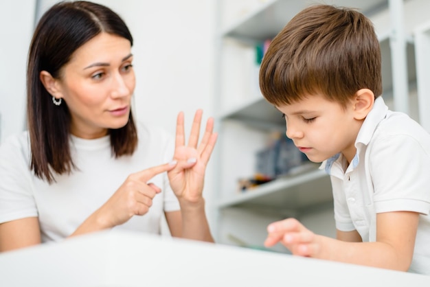 Schöne Logopädin lehrt Jungen die richtige Aussprache von Wörtern und Tönen im Büro