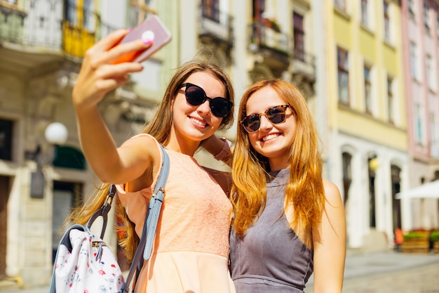 Schöne Mädchen an einem sonnigen Sommertag machen Selfie vor dem Hintergrund der Stadt