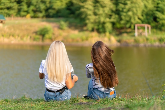 schöne Mädchen genießen die Natur und trinken heißen Tee am Seeufer mit schöner Aussicht