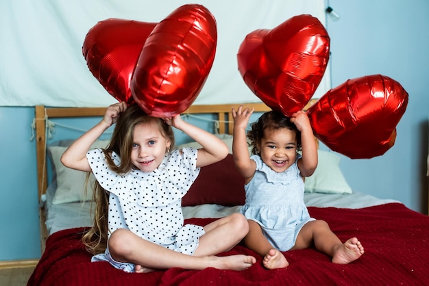 Schöne Mädchen, weiß und mit dunkler Hautfarbe, feiern den Valentinstag. herzförmige rote Folienballons