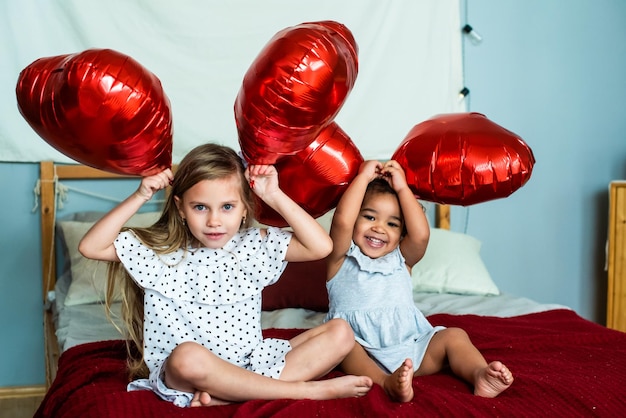 Schöne Mädchen weiß und mit dunkler Hautfarbe feiern Valentinstag herzförmige rote Folienballons