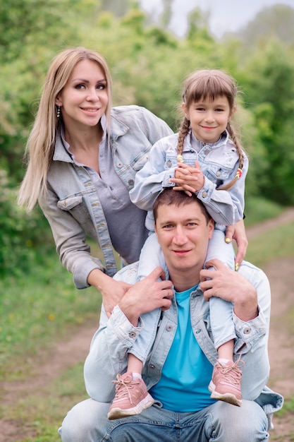 Schöne Mama, Papa und Tochter im Jeans-Outfit gehen im Park spazieren und umarmen sich im Sommer