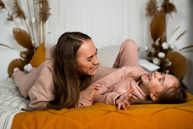 Schöne Mama und Tochter liegen auf einer Decke auf dem Bett und spielen