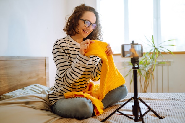 Schöne Modebloggerin, die verträumt einen gelben Pullover hält und ein neues Video für Vlog Online aufnimmt