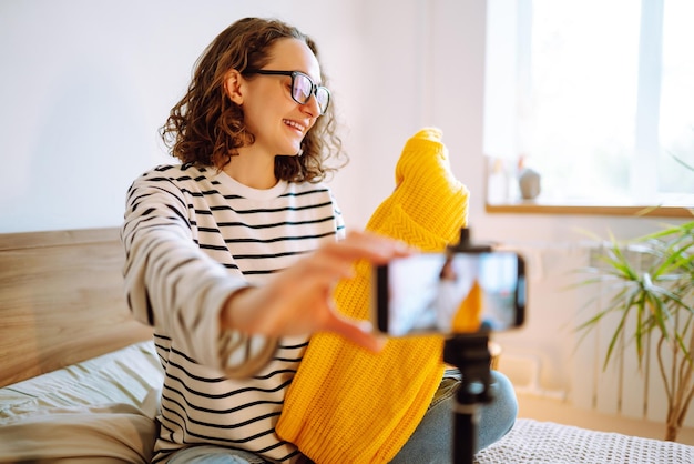 Schöne Modebloggerin mit gelbem Pullover, die träumerisch Videos für Vlog Online-Marketing aufnimmt