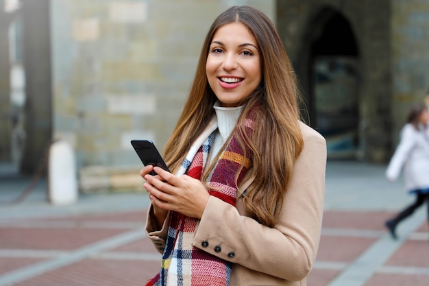 Schöne Modefrau unter Verwendung des Smartphones, das Kamera draußen in der Stadtstraße betrachtet