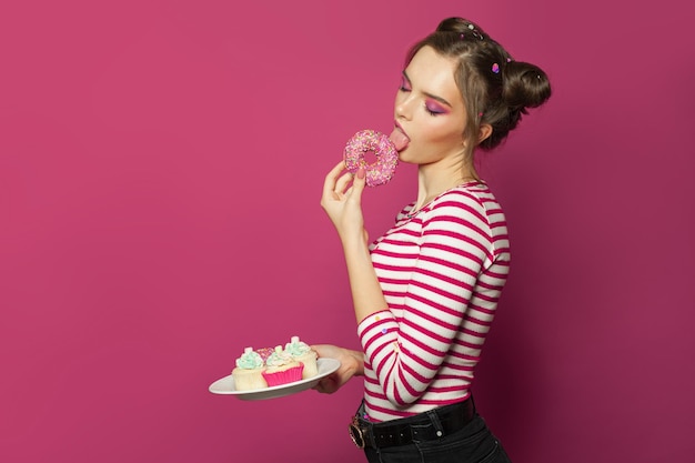 Schöne Modelfrau genießt einen Donut auf buntem rosa Hintergrund