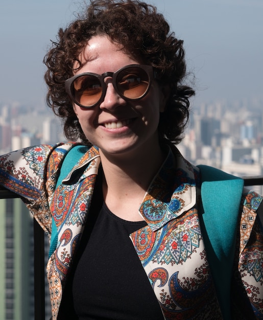 Schöne, moderne Frau, die für Kamera trägt, die Sonnenbrille mit Sao Paulo City im Hintergrund trägt.