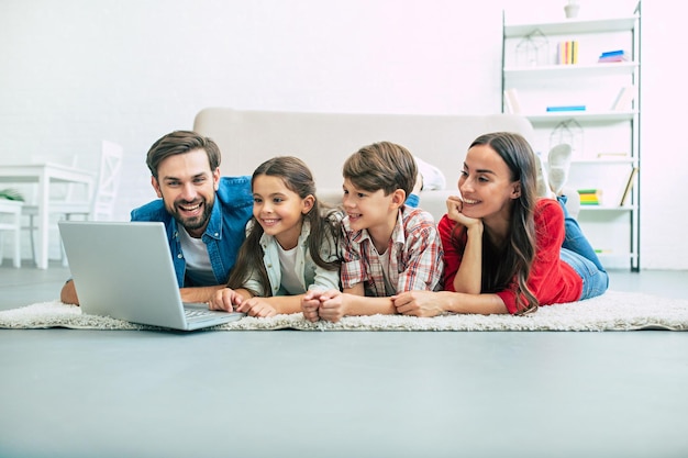 Schöne moderne junge Familie, die zu Hause auf dem Boden liegt und etwas im Laptop macht