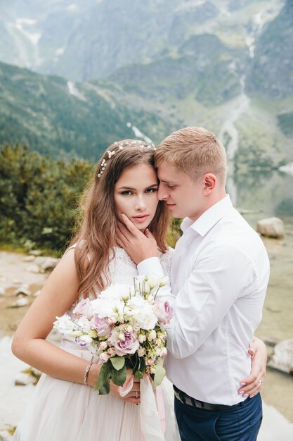 Schöne moderne Paare in der Nähe eines Sees in den Bergen machen Hochzeitsfotos