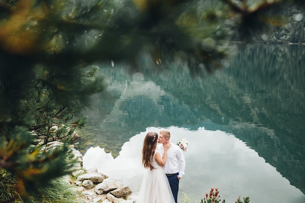 Schöne moderne Paare in der Nähe eines Sees in den Bergen machen Hochzeitsfotos