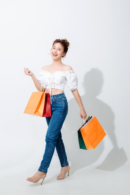 Schöne modische asiatische Frau mit Einkaufstüten stehend isoliert auf weißem Hintergrund und Kopierbereich Einkaufen online bezahlen Lächeln gute Laune