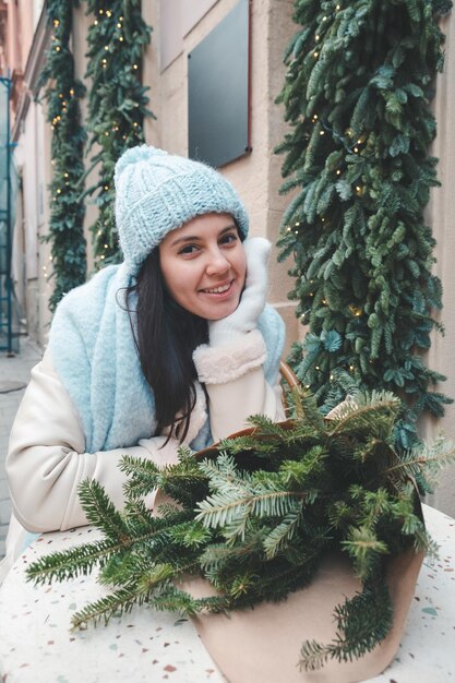 Schöne modische Frau, die auf dem Stuhl im Café im Freien mit Weihnachtsbaumstrauß sitzt