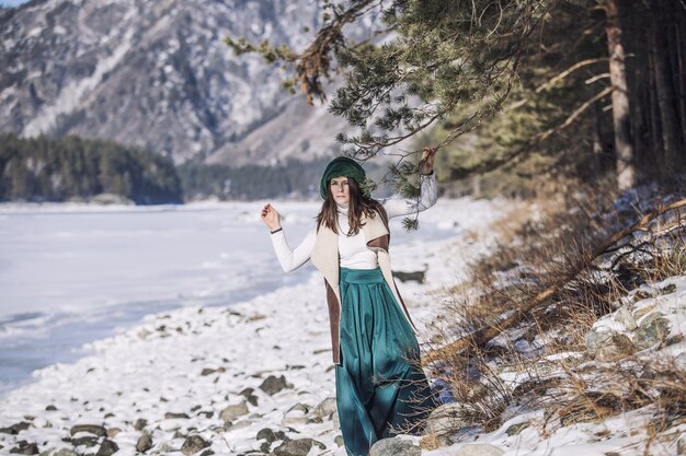 Schöne modische junge Frau im Winter auf einem Hintergrund von Bergen und Flüssen