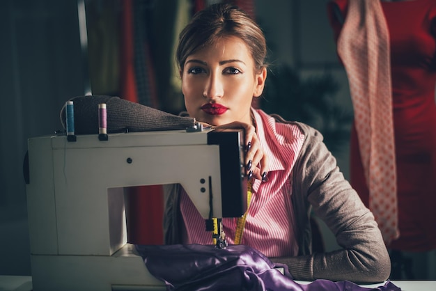 Schöne müde Frau sitzt vor der Nähmaschine und denkt nach. Blick in die Kamera. Vintage-Konzept.