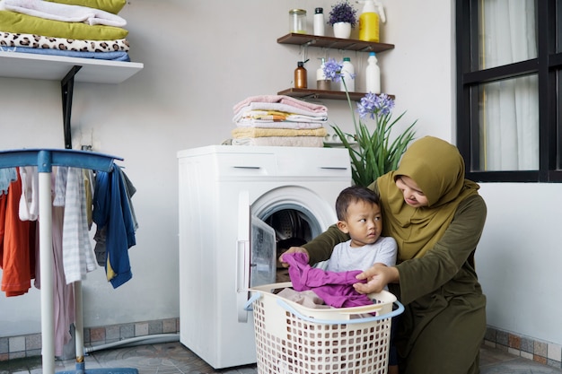 Schöne muslimische asiatische Frau, die Wäsche mit ihrem Sohn zusammen macht