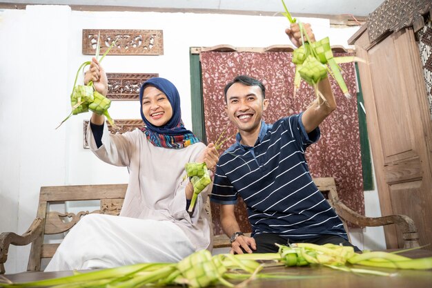 Schöne muslimische Familie und Freunde, die zu Hause Ketupat-Reiskuchen mit Palmblättern für die Eid Fitr Mubarak-Tradition herstellen