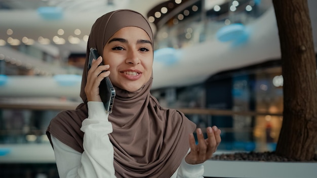 Schöne muslimische Frau im Hijab, die in der Öffentlichkeit sitzt, telefoniert mit dem Handy im Einkaufszentrum, weiblich