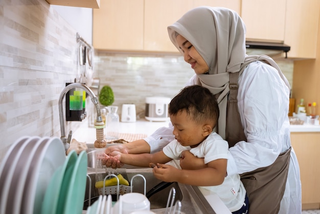 Schöne muslimische Mutter waschen ihre Sohnhand im Küchenspülbecken