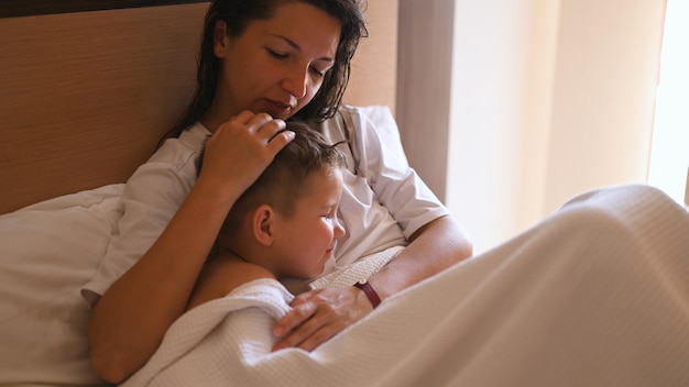 Schöne Mutter, die Sohn ins Bett legt Glückliches Familienkonzept Foto in hoher Qualität